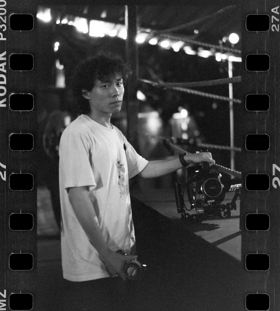 Kenn Zhengchuan Mei on set beside a rigged cinema camera, shot on Kodak P3200 film